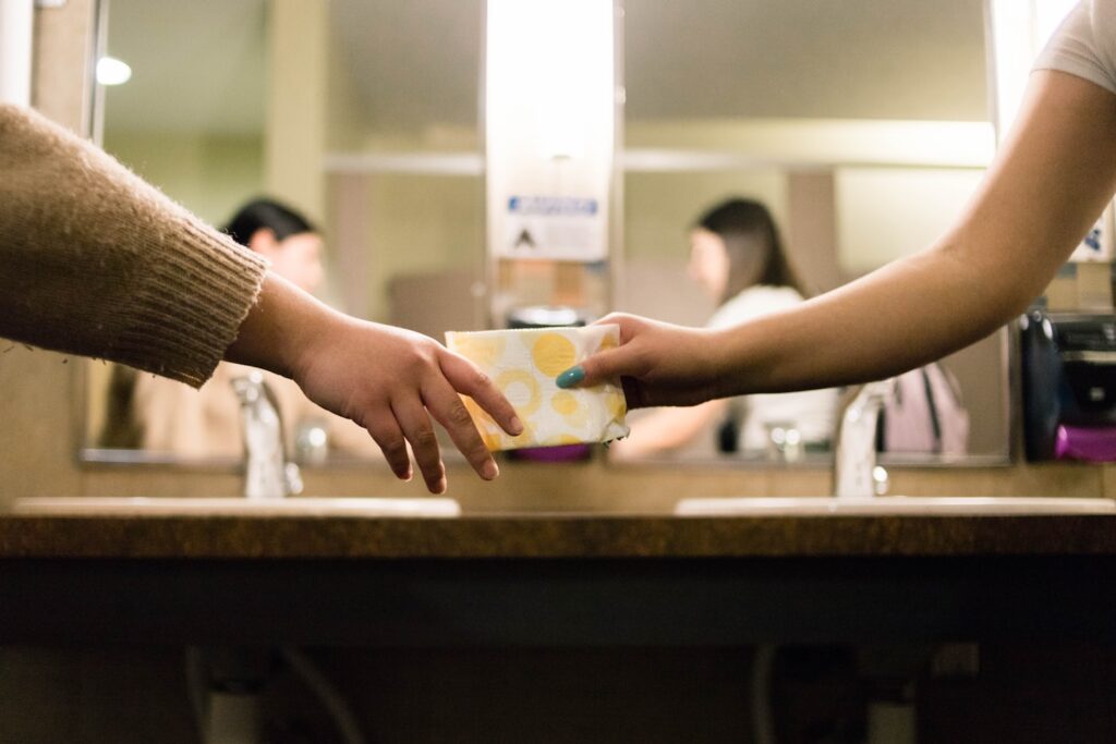 A woman passes a menstrual product to another.