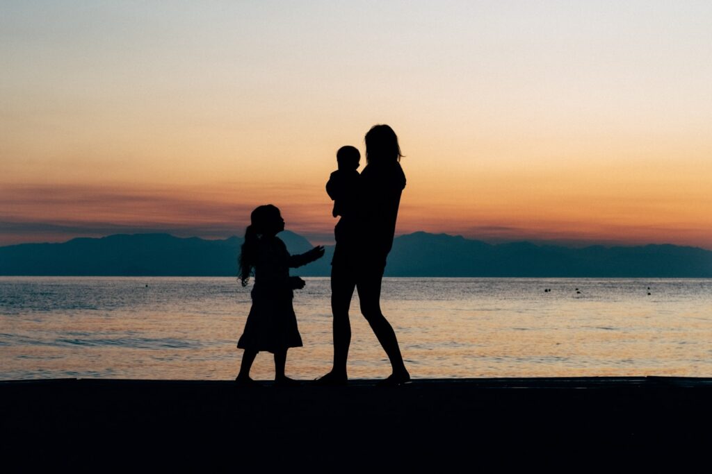 A family of three. Brother, sister and mother, stroll on the beach in Greece at sunrise. When the kids can't sleep on holiday, take them for a walk on the beach. If you can wake up it makes great photos for the golden hour.