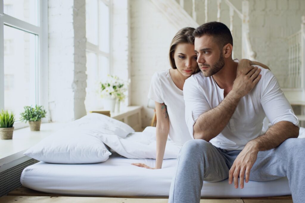 Depressed yong man sitting in bed having stressed while his girlfriend come and embrace him in bedroom at home